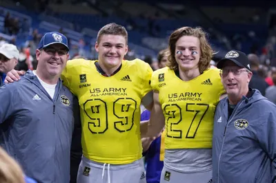 Left to right: Wilsonville Head Coach Adam Guenther in a W cap, Draco Bynum in a yellow U.S. Army All-American No. 99 jersey, Chase Cota in No. 27, who played for South Medford and then UCLA, and South Medford Head Coach Bill Singler, smiling on the field at the U.S. Army All-American Bowl
