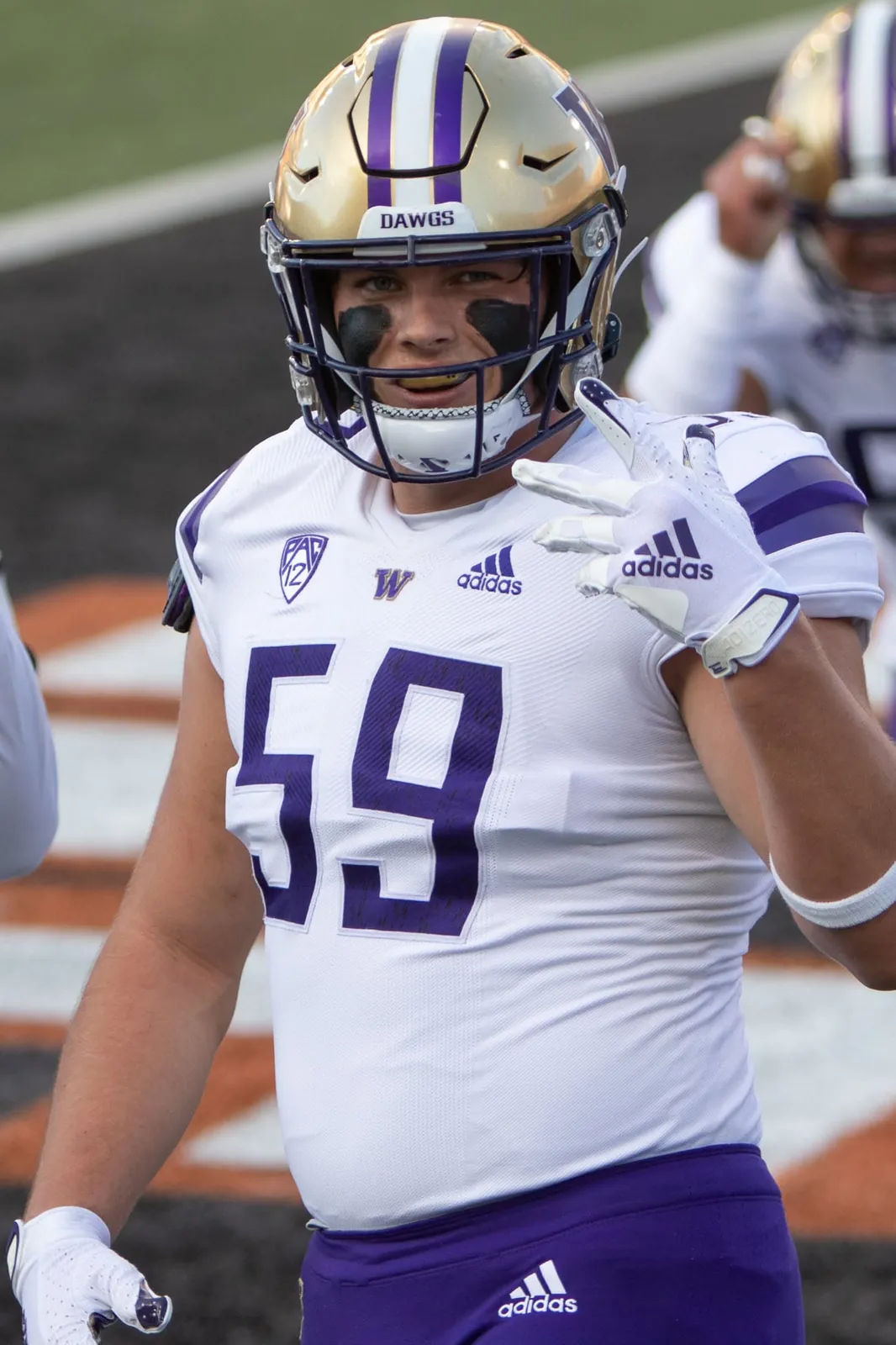 Draco Bynum in a white Washington No. 59 jersey and gold helmet, waving on the field