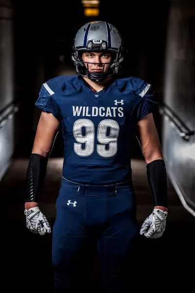 Senior football portrait of Draco Bynum in a navy Wildcats No. 99 uniform and helmet, standing in a tunnel