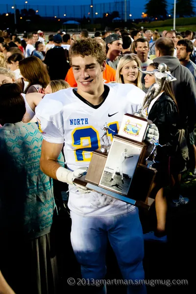 Tanner Shipley, smiling in a white North No. 21 jersey, holding a trophy among a crowd on the field after the 2013 Les Schwab Bowl