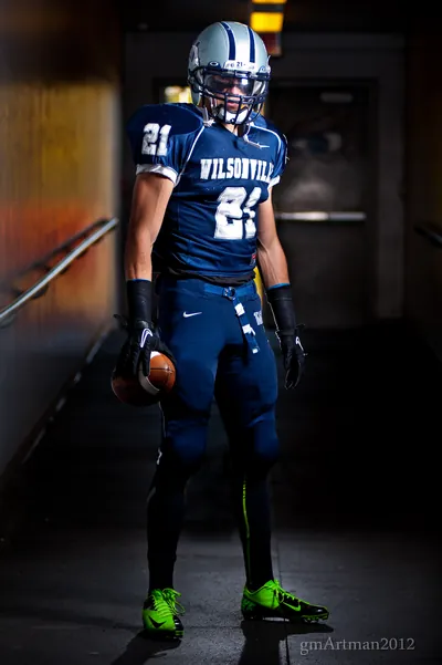 Posed portrait of Tanner Shipley in a stadium tunnel in his navy Wilsonville No. 21 uniform and silver helmet, holding a football, 2012