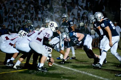 Andrew Walls, Wilsonville No. 76 in navy, in a three-point stance at the line of scrimmage at a night game in front of a crowd dressed in white, 2011