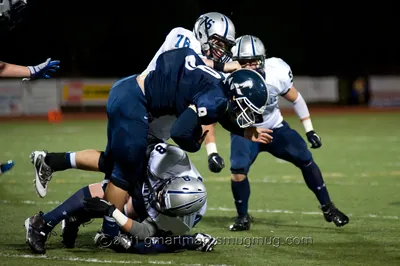 Andrew Walls, No. 76 in a white Wilsonville away jersey, wrapping up a ball carrier in a navy uniform at a night game, 2011